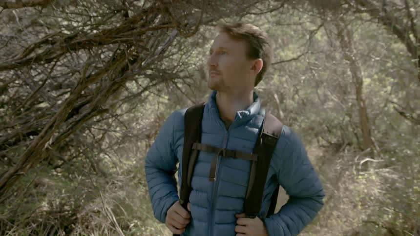 A man is smiling as he hikes in the woods