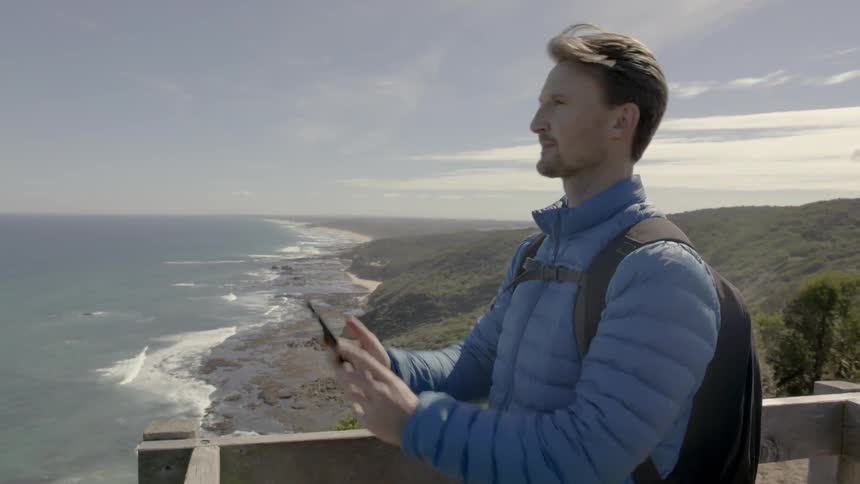 A man takes a photograph with a smartphone on the coast