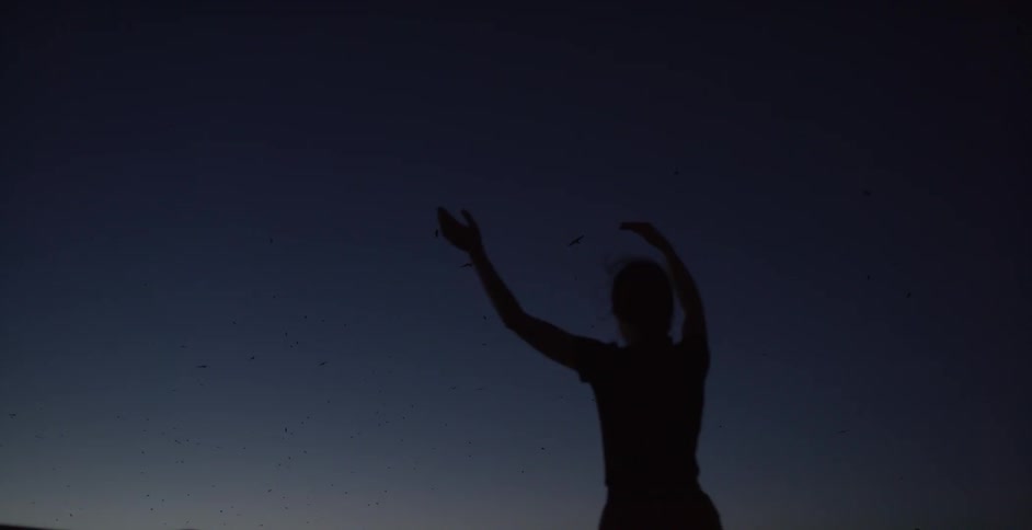 A woman stretches her arms upwards outside at night