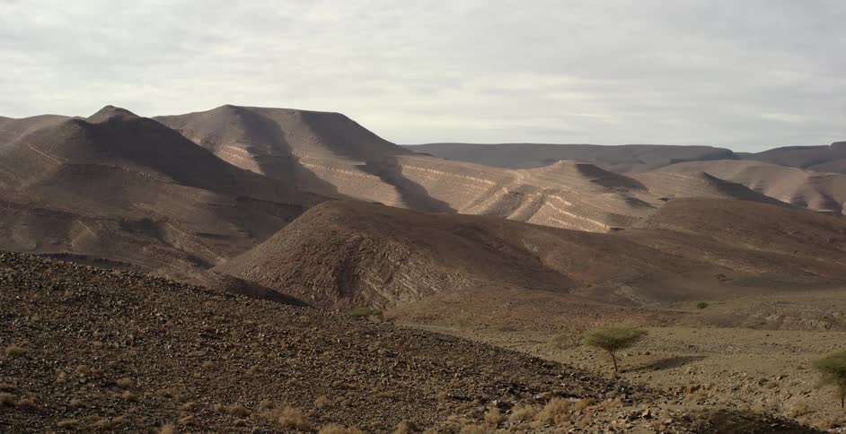 Hills rise in a desert beneath cloudy skies