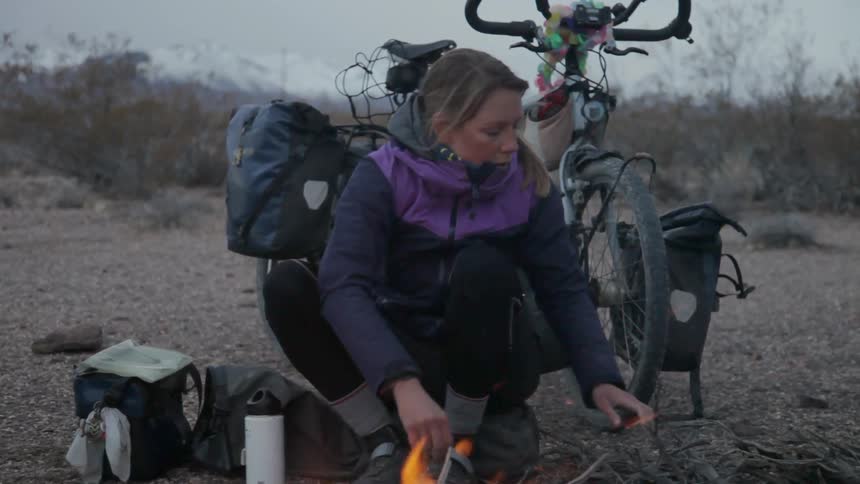A woman is putting wood into her campfire