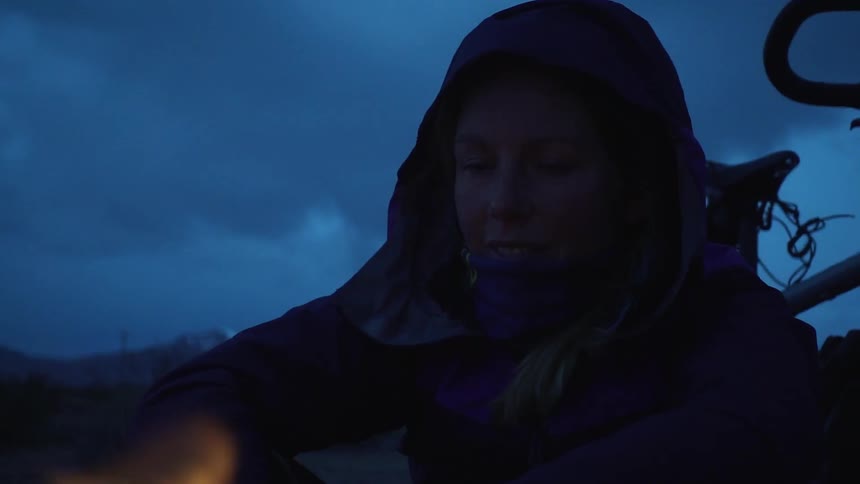 A woman sits by the fire at dawn