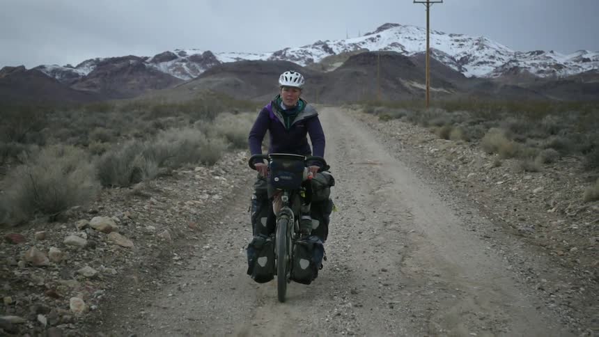 A woman bicycles on a dirt road in the mountains