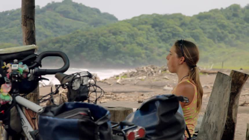 A woman sits next to a bike on a shoreline