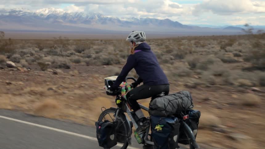 A woman bicycles towards a mountain range
