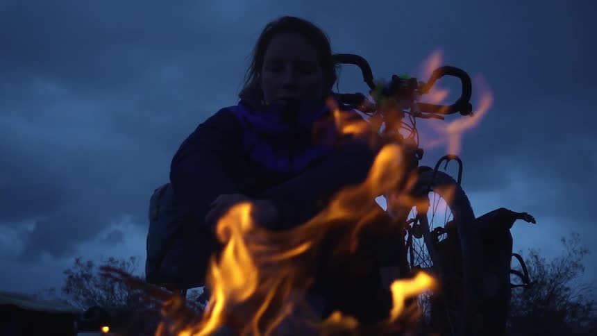 A woman sits in front of a fire on a cloudy day