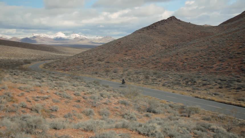 Person on a motorcycle travels on a road through a barren hilly desert