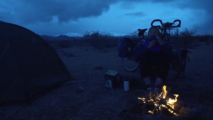 Person sitting in front of a fire in nature in the evening