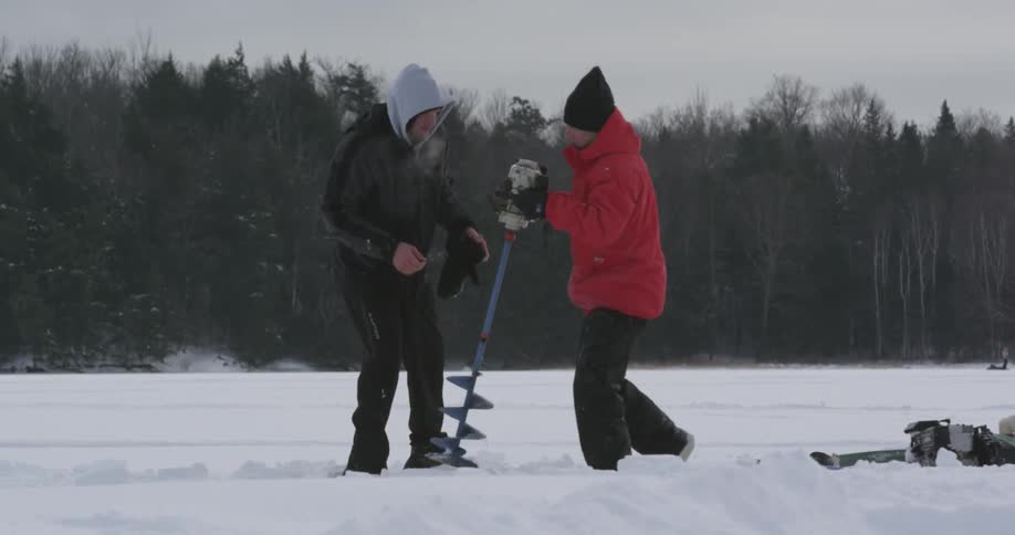 Two people pull a drill up out of the snow