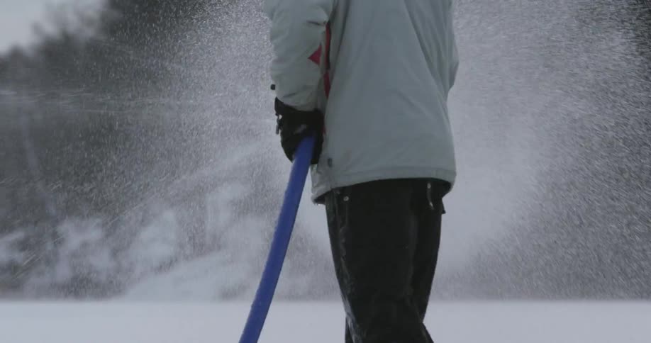 Man spraying a large hose over a snow covered area
