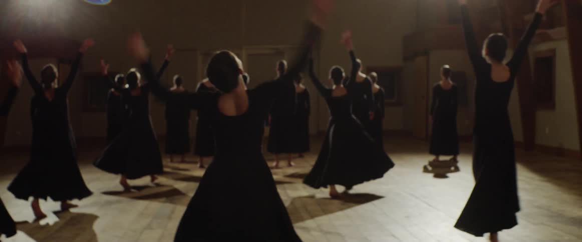 Women in black dresses dance together in a hall