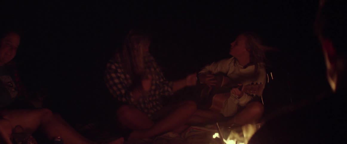Girls sing and play guitar around a campfire