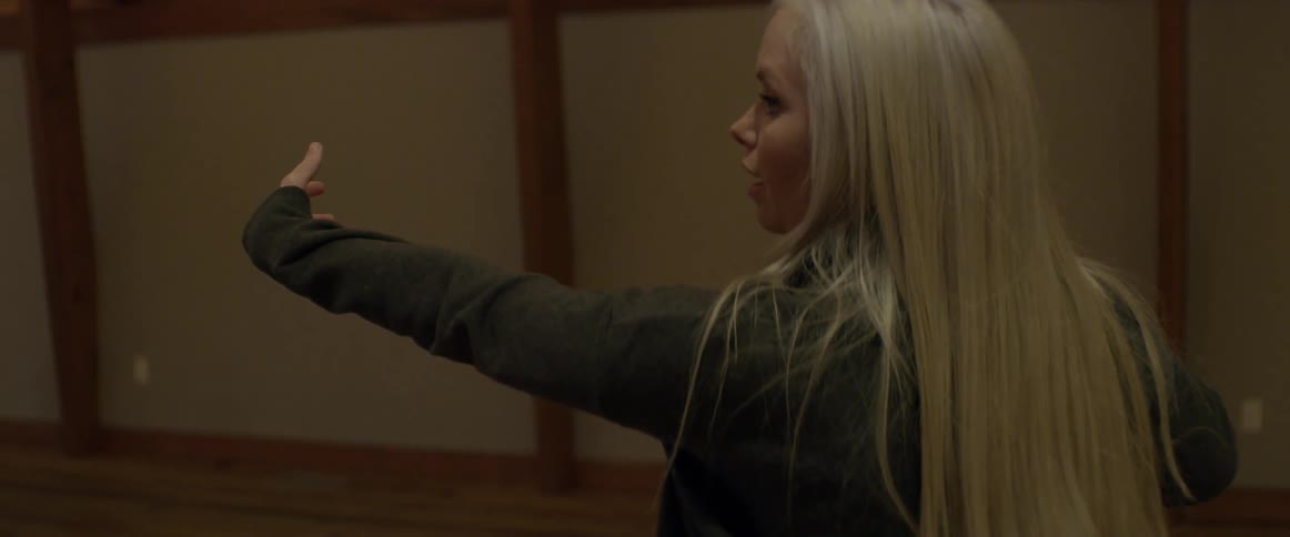 A blonde woman gestures toward a class