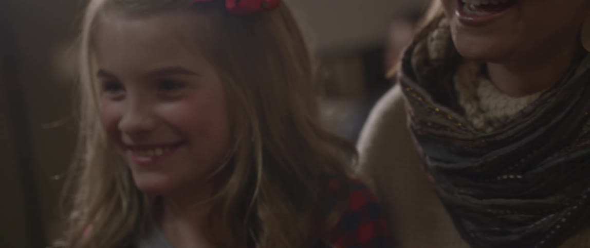 Smiling girl with a red bow sitting next to her mother that is talking to someone