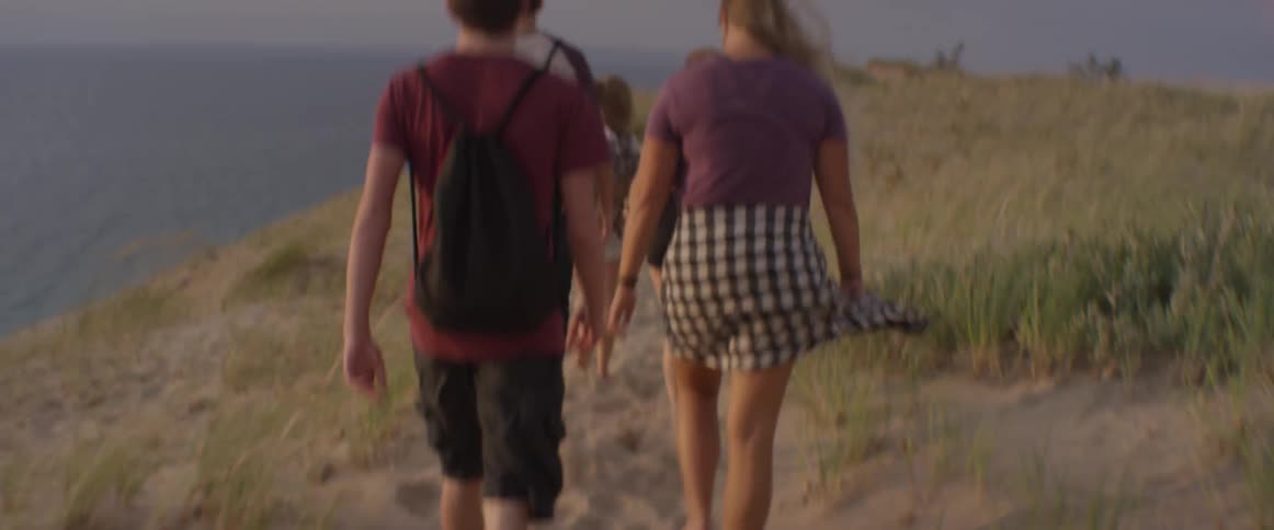 People walk barefoot on the beach with a dog