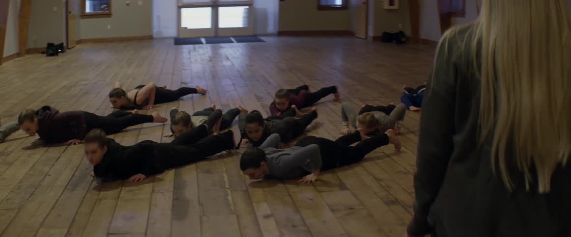 Men and women dancing in a line with an instructor watching