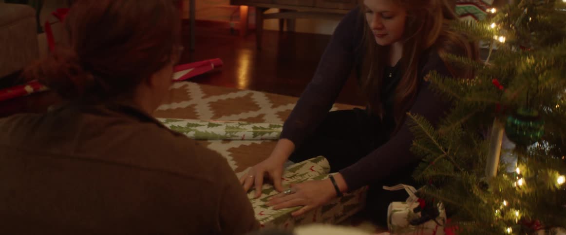 Two women wrap presents next to a tree