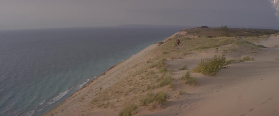 People walk on a sand hill near a lake