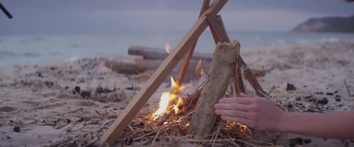 Two people work on building a campfire on the beach