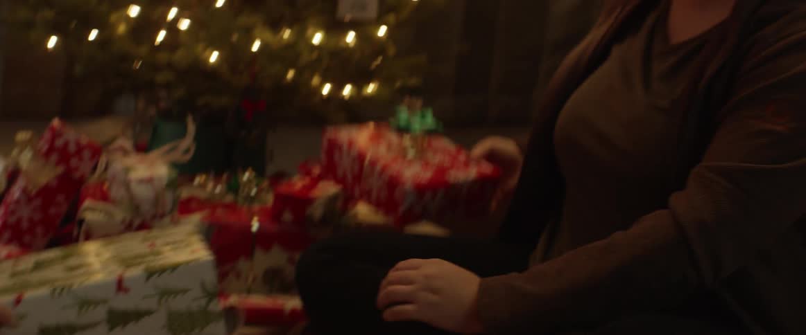Woman puts a bow on a present and puts it underneath the tree