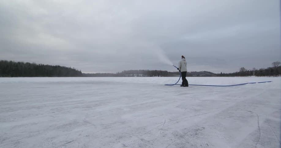 A white man sprays water on a frozen lake with a large hose