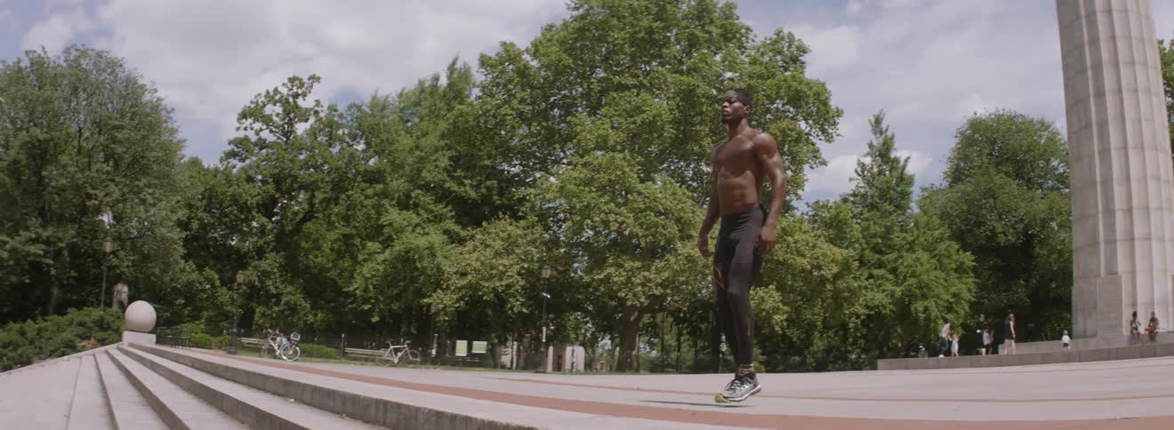 A shirtless man warms up by bouncing in a park
