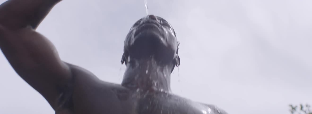 A shirtless man pours water over his head