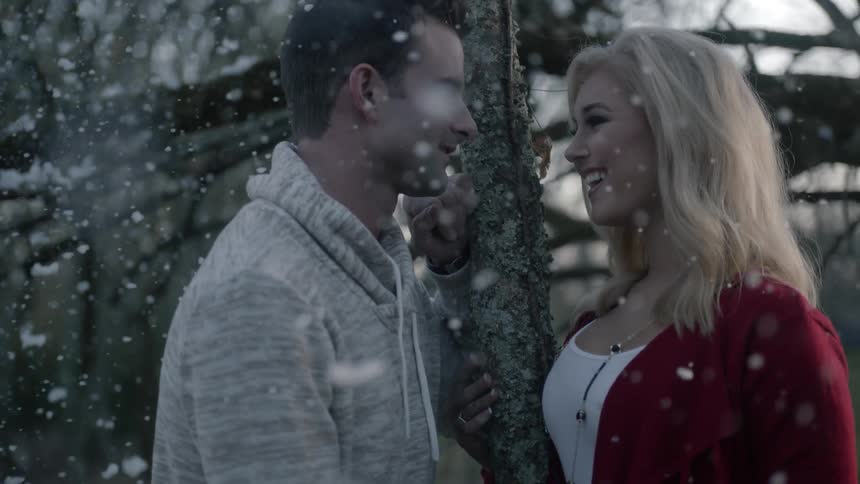 A man and woman stand near a tree in the snow and talk