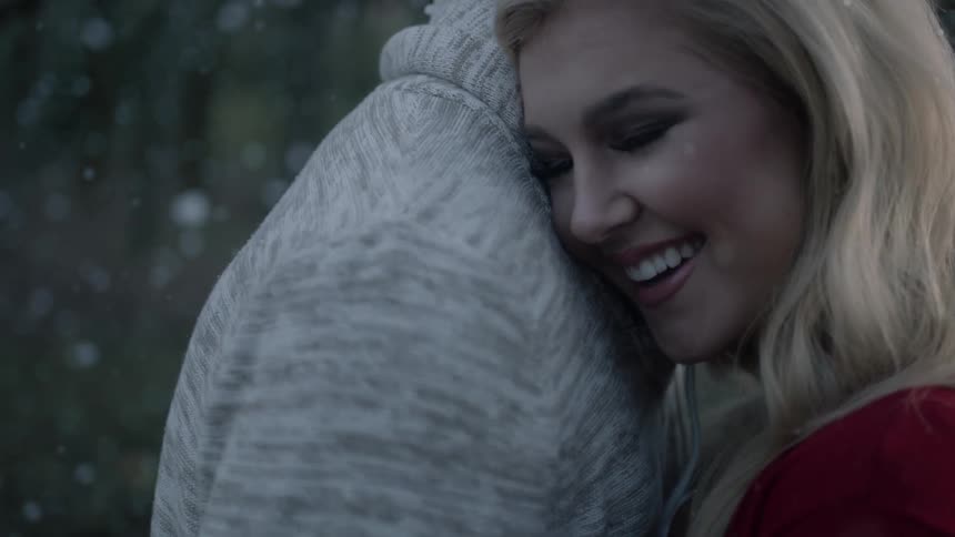 A blonde woman smiles and laughs while slow dancing with a man in the snow