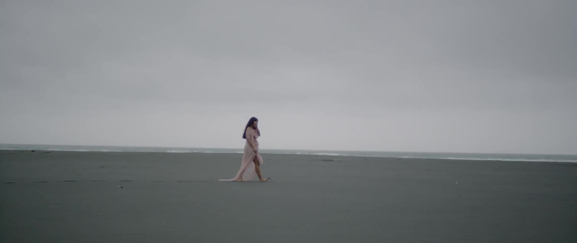 Woman wearing a long flowing dress walks in the sand