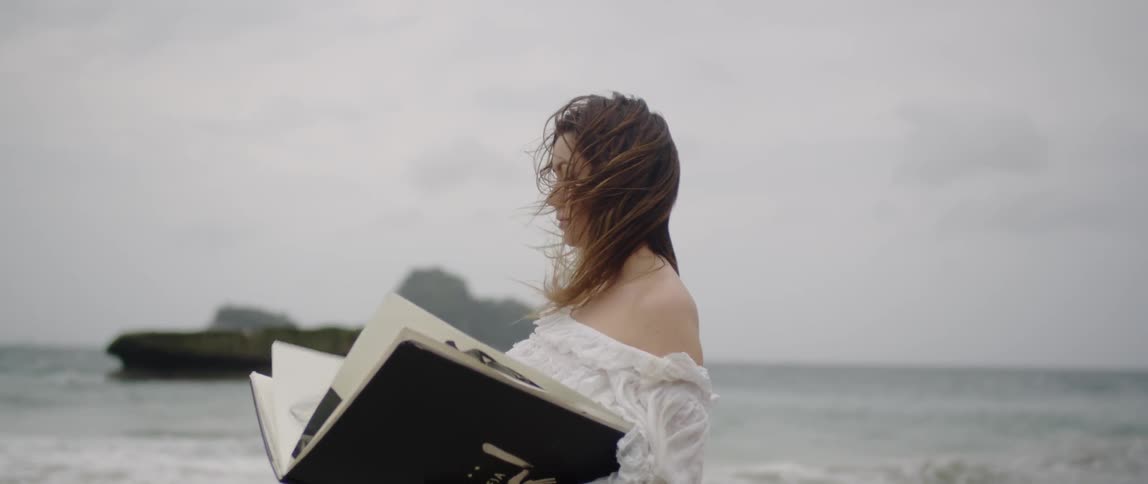 A woman is standing on the beach holding a large book