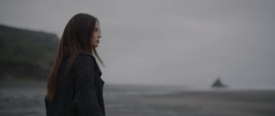 A woman wearing a sweater walks on the beach