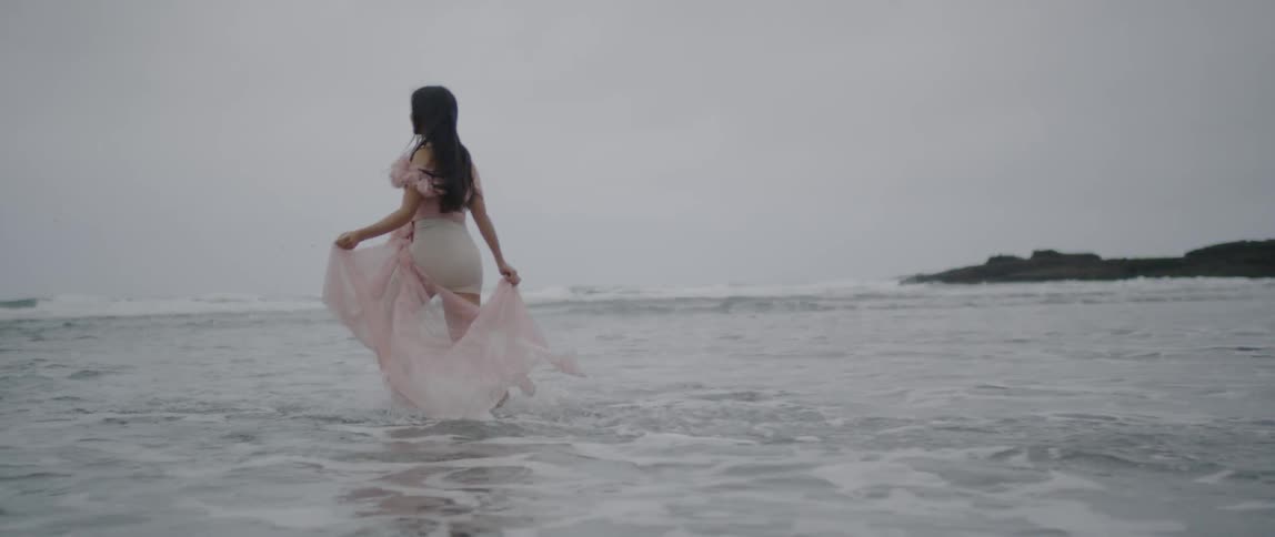 A woman in a pink dress runs in the beach water