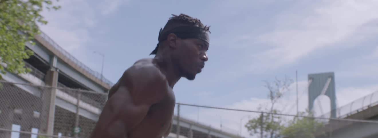 A shirtless man runs and jumps over a net