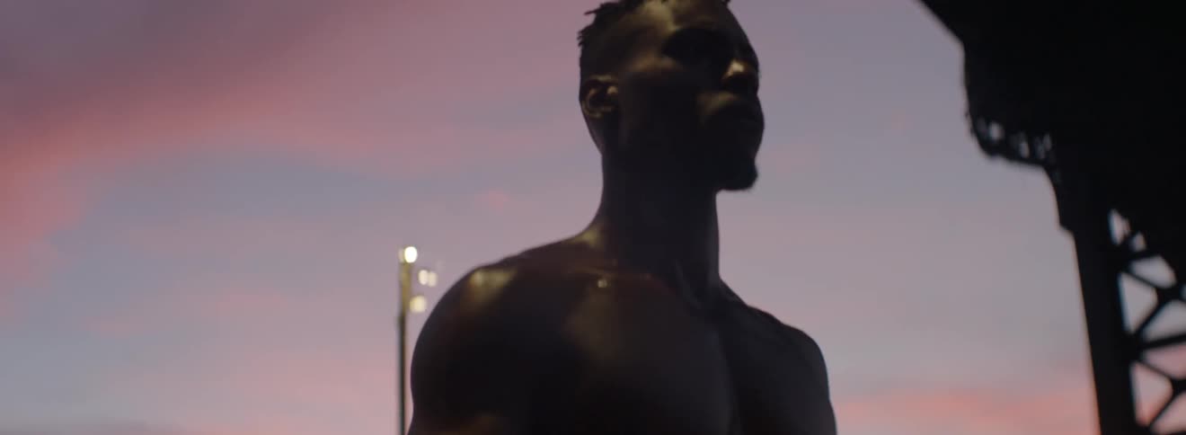 A shirtless man walks beneath a city overpass at sunset