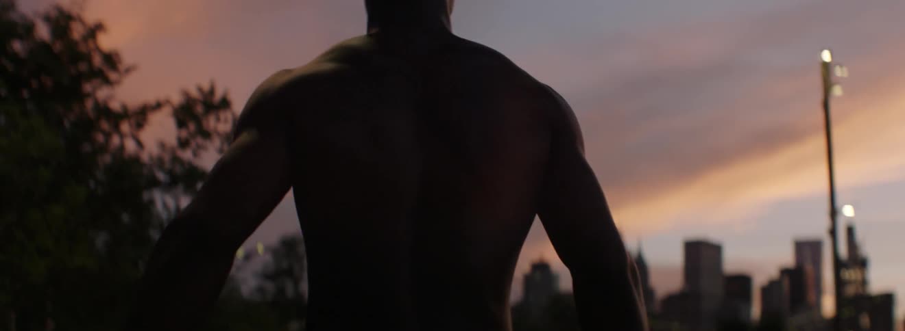 Shirtless man stands outside at sunset