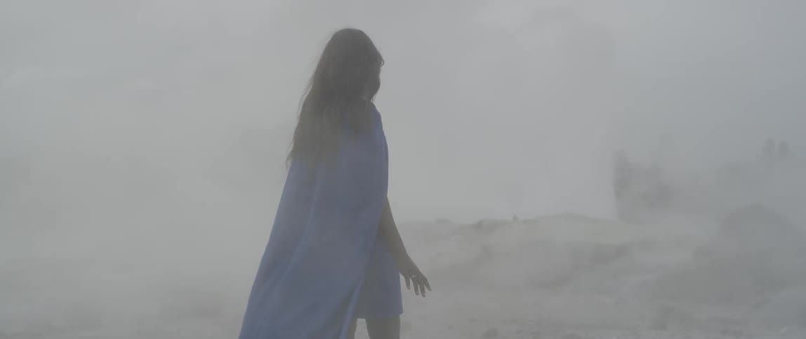 A woman wearing a blue cape stands in the billowing mist