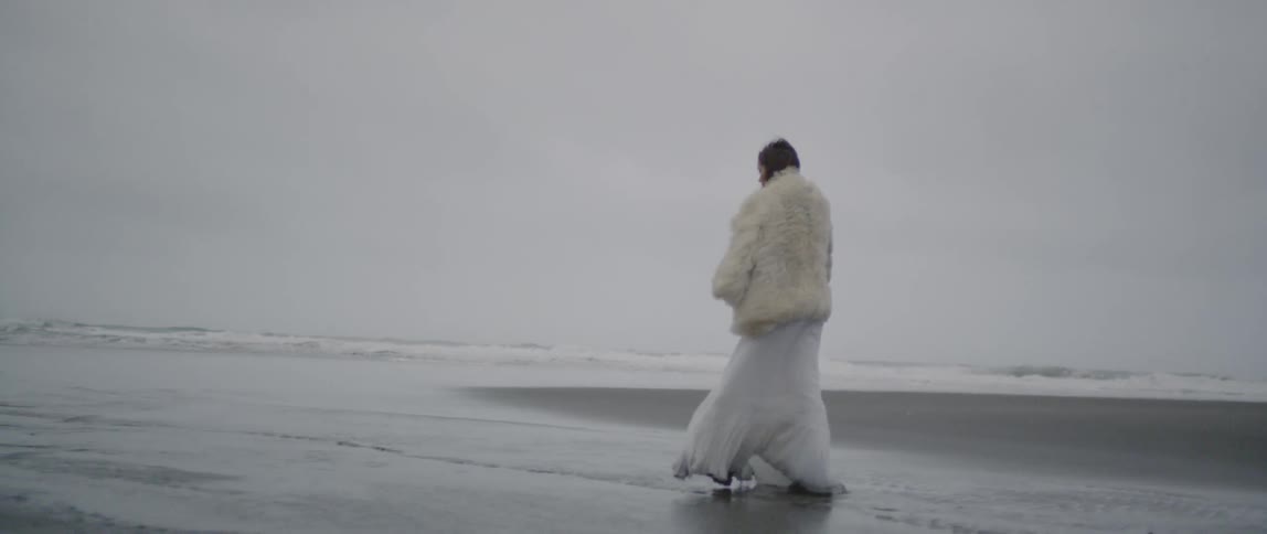 A woman in white is walking along the beach