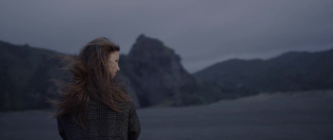 A woman stands along the shore as the wind blows her hair