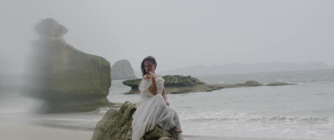A woman in a white dress sits on the rocks