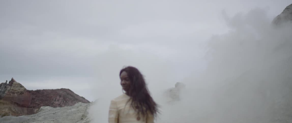 A woman walks near steam outside on a cloudy day