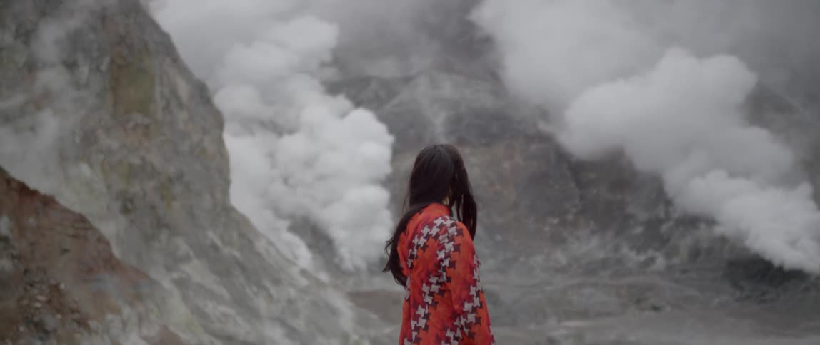 A woman stands watching steam rising from the ground