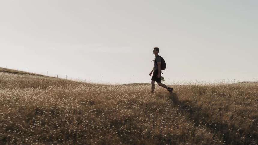 A man hikes across a grassy field