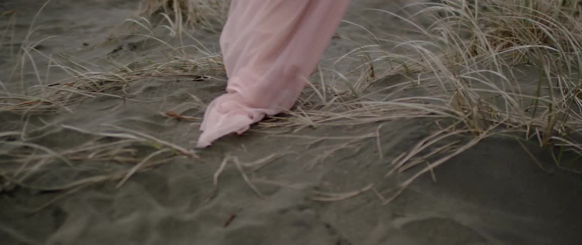 A woman in a sheer white dress walks in the sand