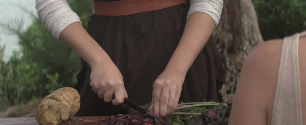 Young girl uses a knife to slice a vegetable