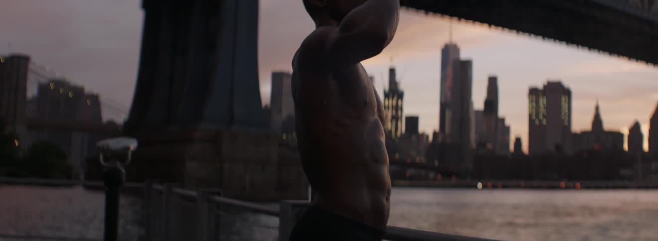 A shirtless man drinks a bottle of water and dumps it over his face