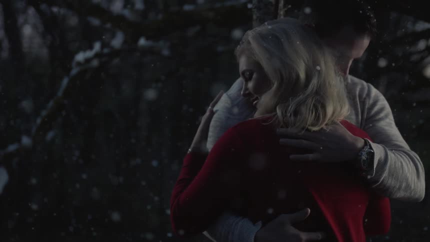 Man and woman kiss and embrace as it snows