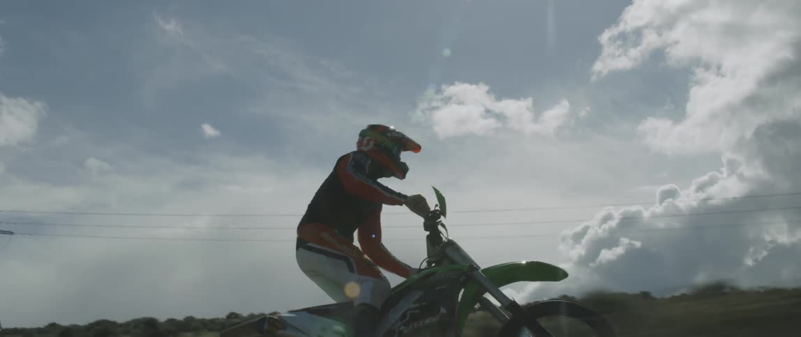 Someone rides a dirt bike through a field under the bright sun