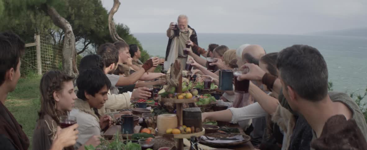 A large group of people raise their glasses in a toast while dining outside