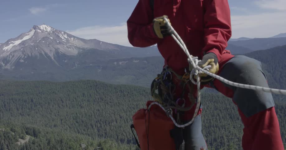 A man tightens up a rope harness on the side of a mountain